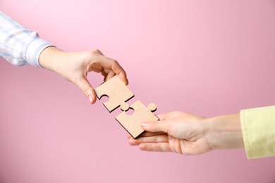 Photo of Business strategy and teamwork concept. Partners putting puzzle pieces together on pink background, closeup