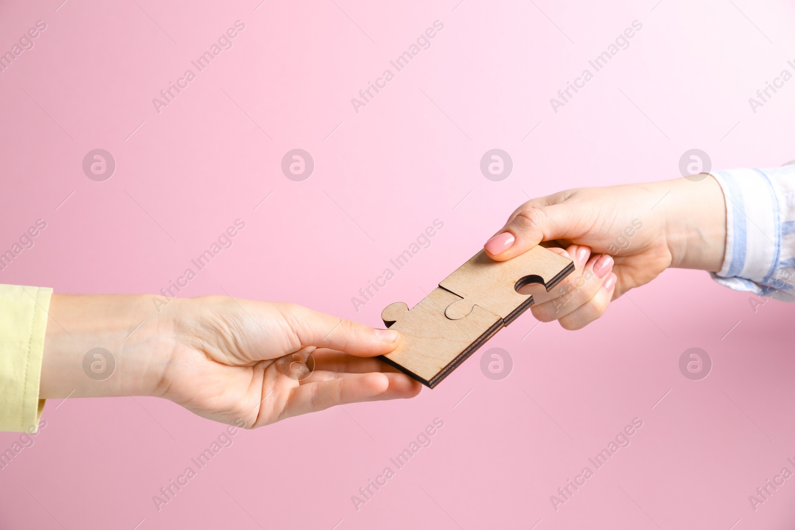 Photo of Business strategy and teamwork concept. Partners putting puzzle pieces together on pink background, closeup