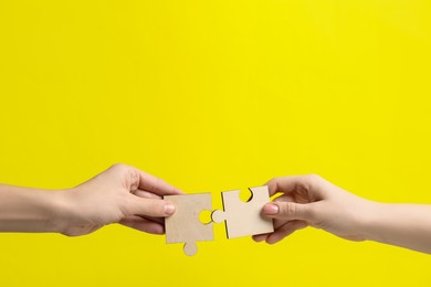 Photo of Business strategy and teamwork concept. Partners putting puzzle pieces together on yellow background, closeup. Space for text