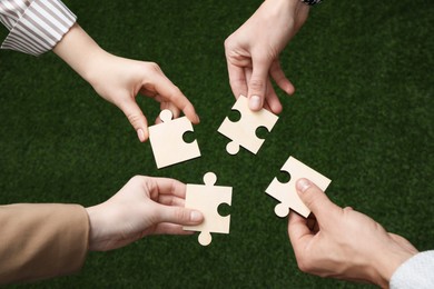 Photo of Teamwork. Group of people putting puzzle pieces together on blurred background, top view