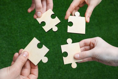 Photo of Teamwork. Group of people putting puzzle pieces together on blurred background, top view