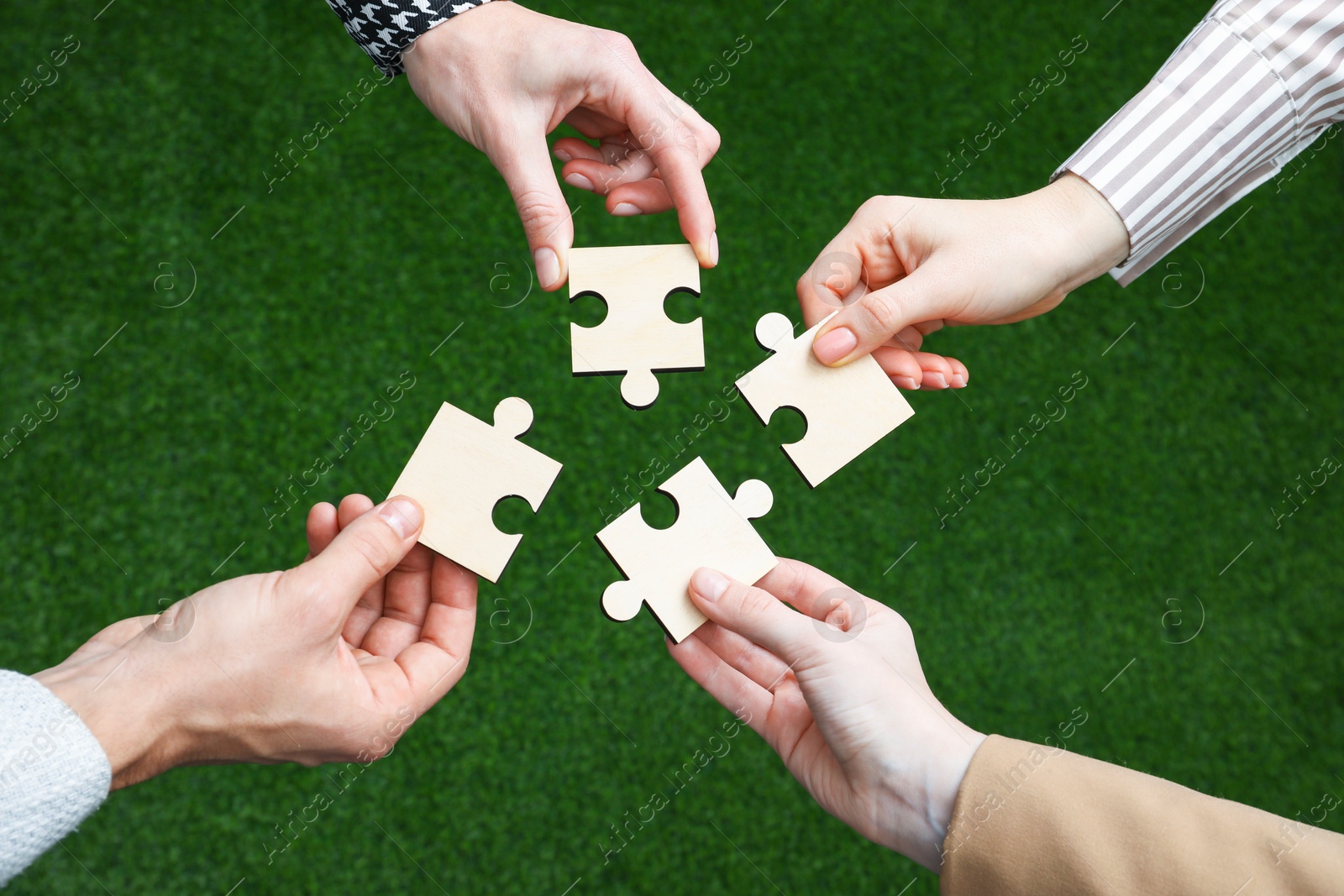 Photo of Teamwork. Group of people putting puzzle pieces together on blurred background, top view