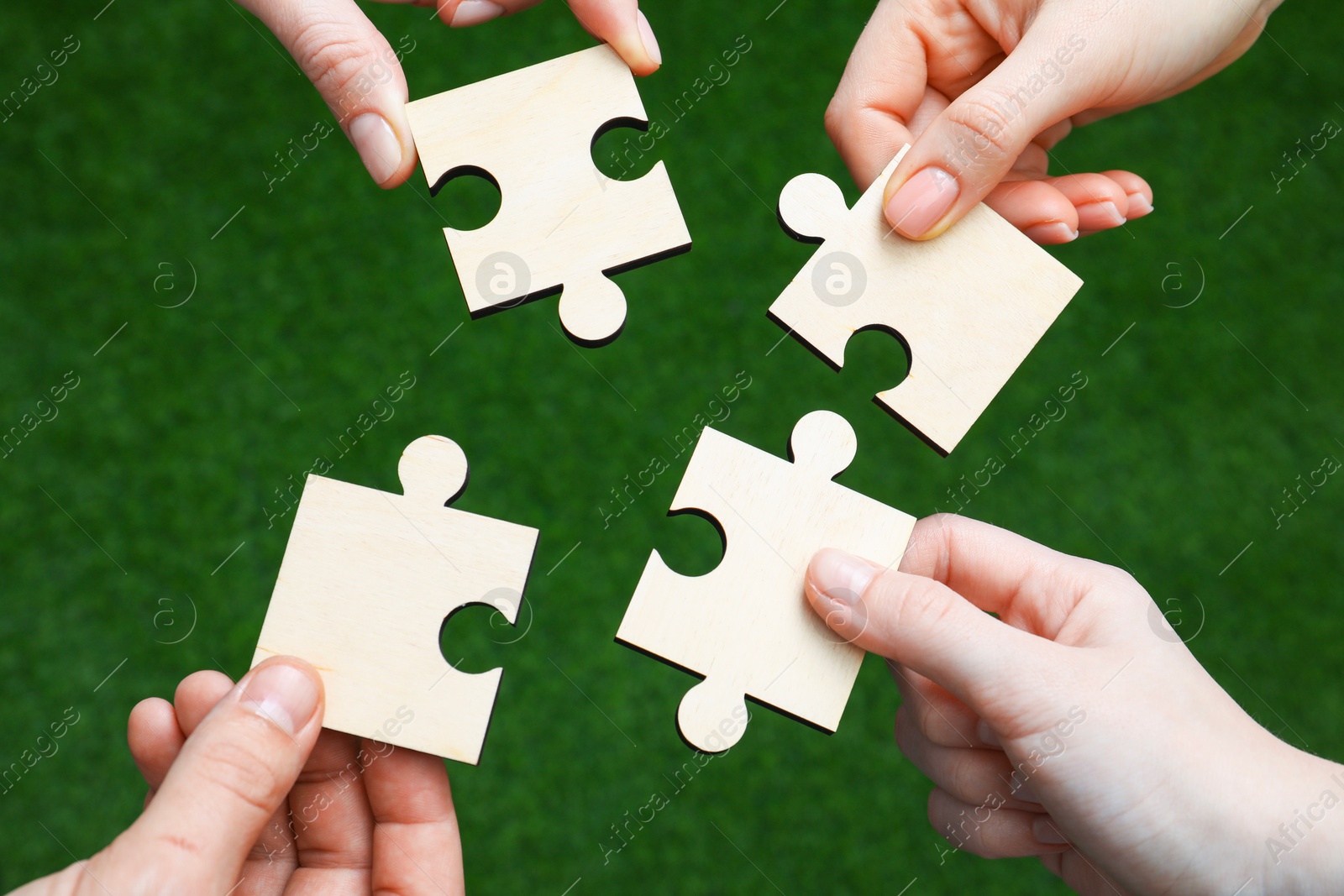 Photo of Teamwork. Group of people putting puzzle pieces together on blurred background, top view