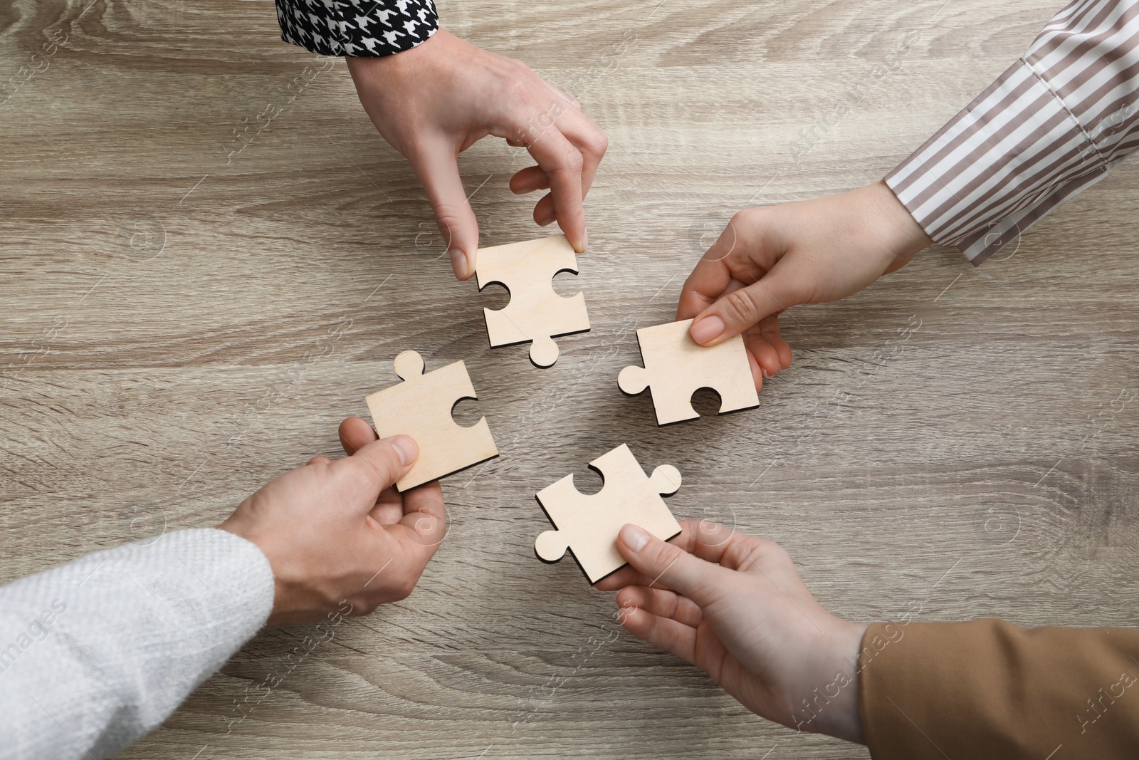 Photo of Teamwork. Group of people putting puzzle pieces together at wooden table, top view