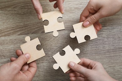 Photo of Teamwork. Group of people putting puzzle pieces together at wooden table, top view