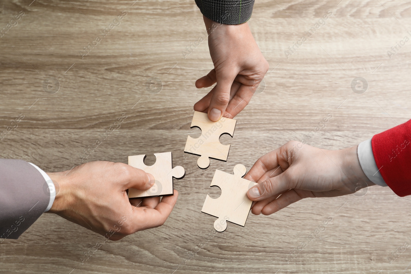 Photo of Teamwork. People putting puzzle pieces together at wooden table, top view