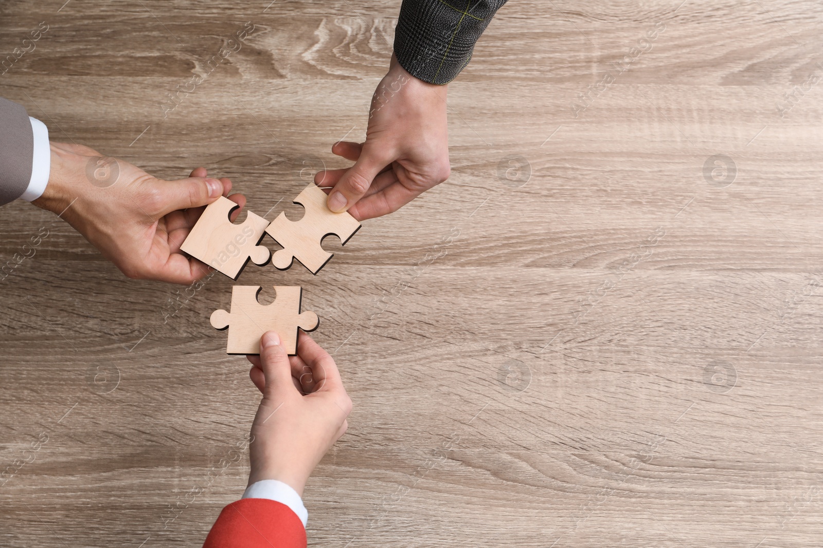 Photo of Teamwork. People putting puzzle pieces together at wooden table, top view. Space for text