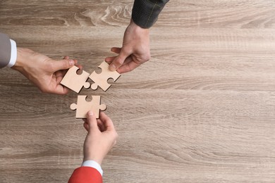 Photo of Teamwork. People putting puzzle pieces together at wooden table, top view. Space for text