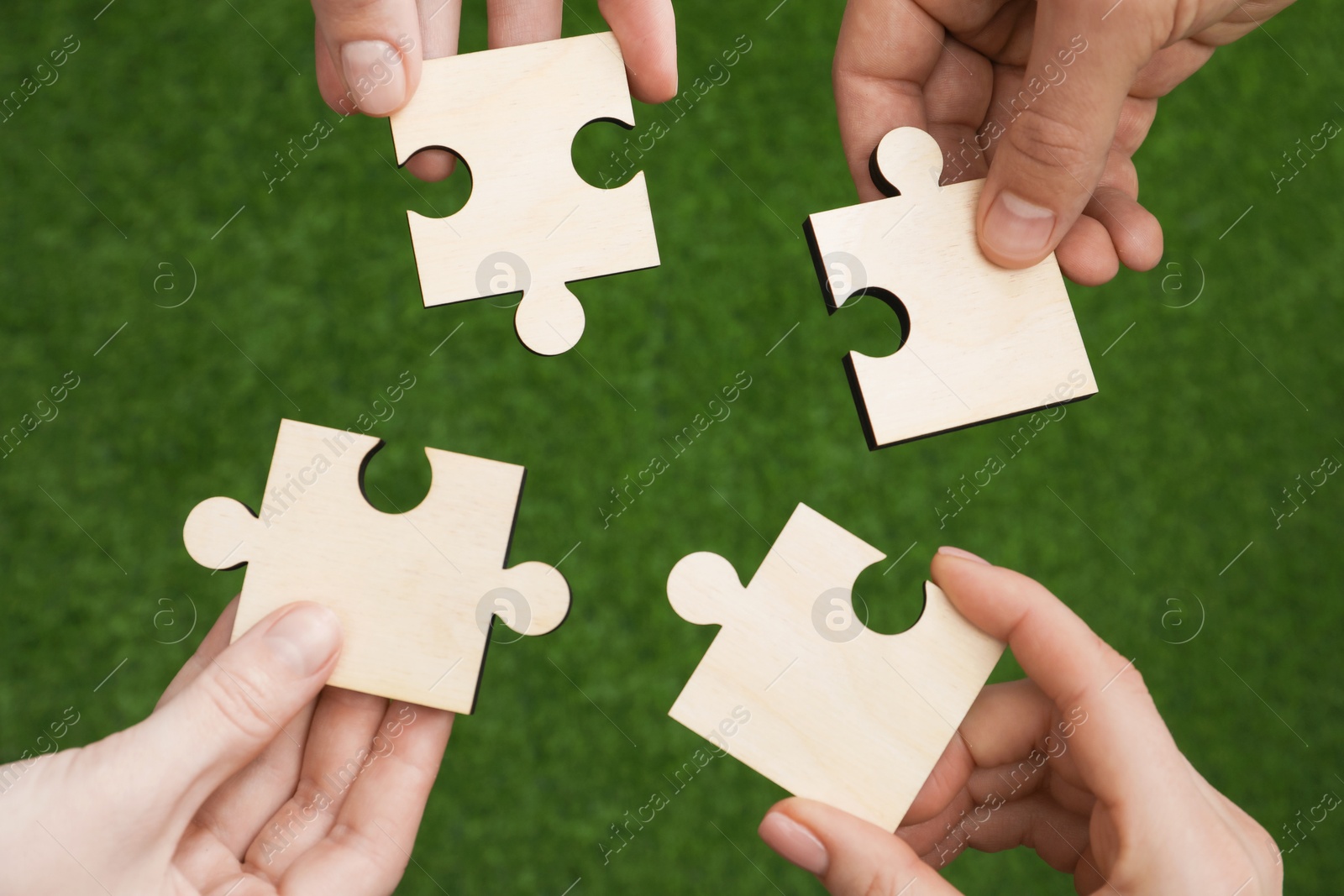 Photo of Teamwork. Group of people putting puzzle pieces together on blurred background, top view