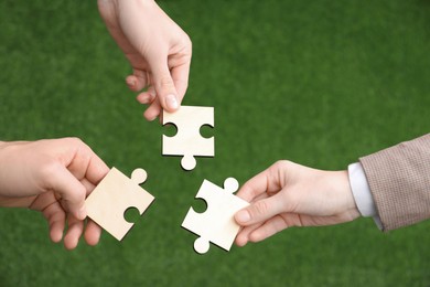 Photo of Teamwork. Group of people putting puzzle pieces together on blurred background, top view