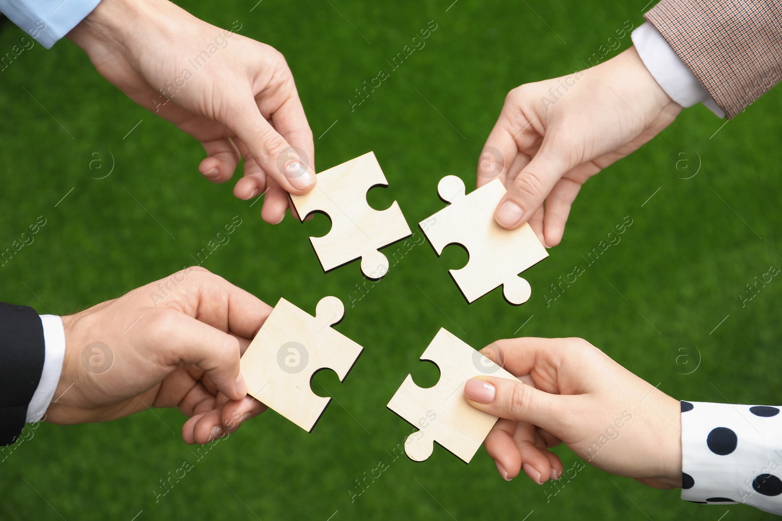 Photo of Teamwork. Group of people putting puzzle pieces together on blurred background, top view