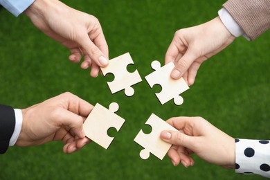 Photo of Teamwork. Group of people putting puzzle pieces together on blurred background, top view