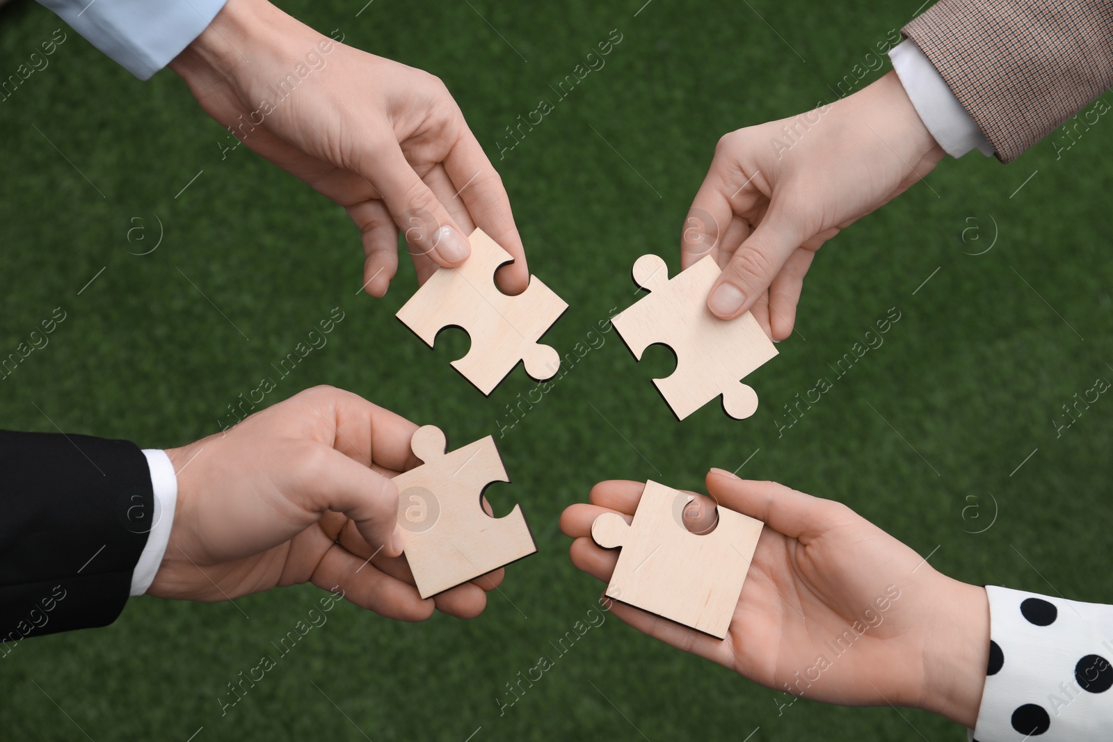 Photo of Teamwork. Group of people putting puzzle pieces together on blurred background, top view