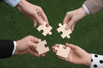 Photo of Teamwork. Group of people putting puzzle pieces together on blurred background, top view