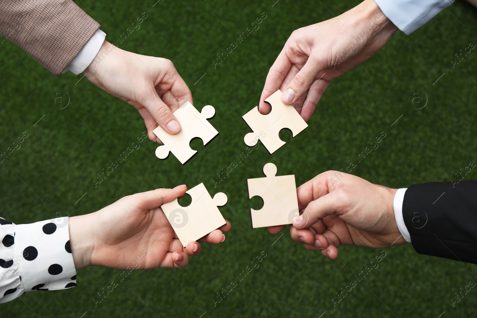 Photo of Teamwork. Group of people putting puzzle pieces together on blurred background, top view