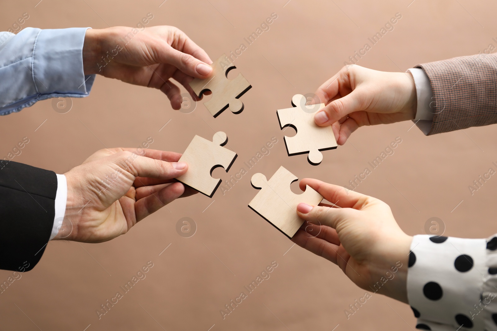 Photo of Teamwork. Group of people putting puzzle pieces together on beige background, closeup