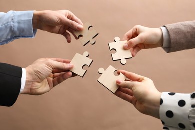 Photo of Teamwork. Group of people putting puzzle pieces together on beige background, closeup