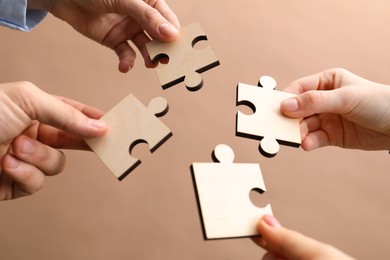 Photo of Teamwork. Group of people putting puzzle pieces together on beige background, closeup