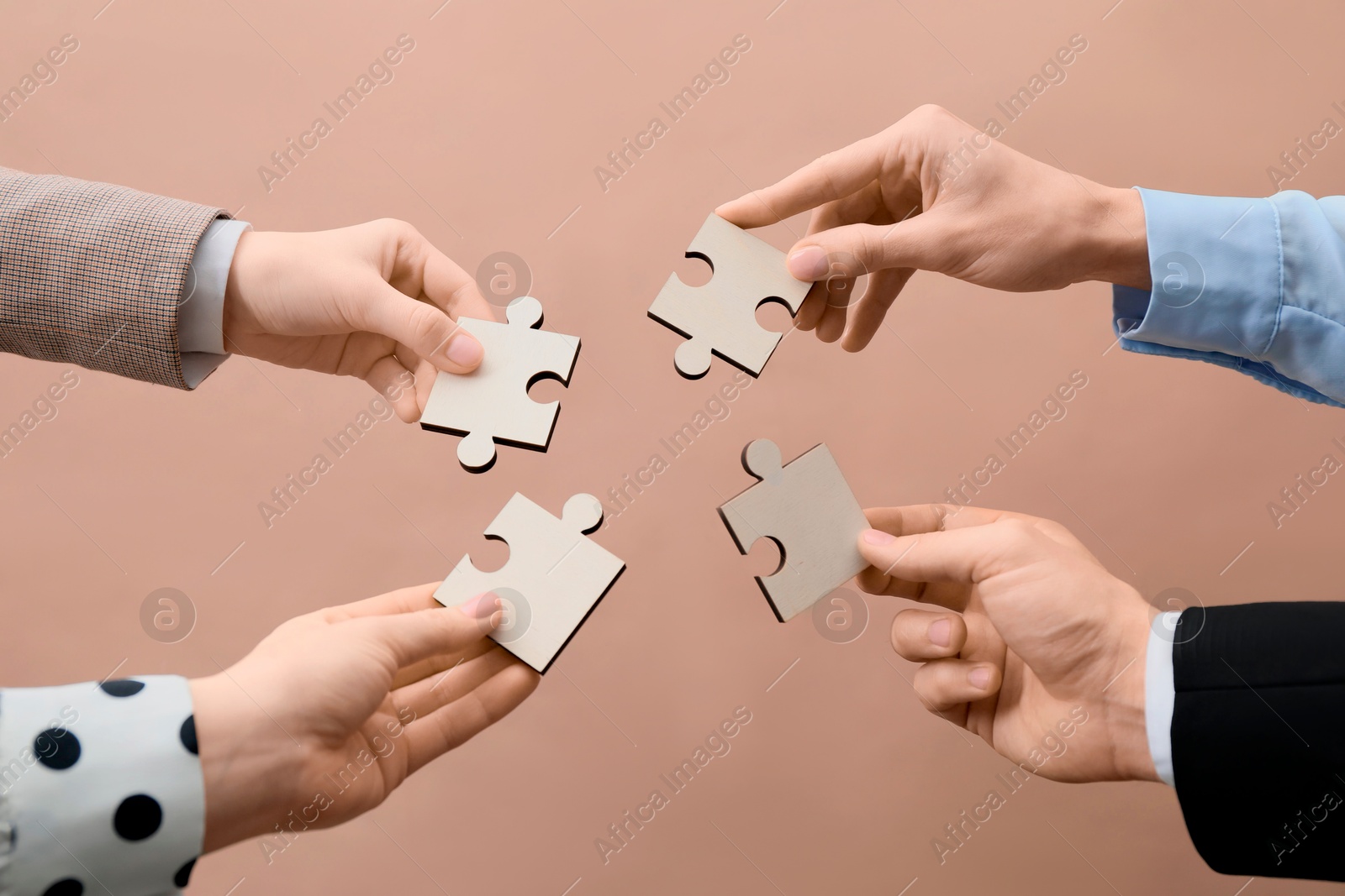 Photo of Teamwork. Group of people putting puzzle pieces together on beige background, closeup