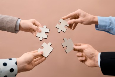 Photo of Teamwork. Group of people putting puzzle pieces together on beige background, closeup