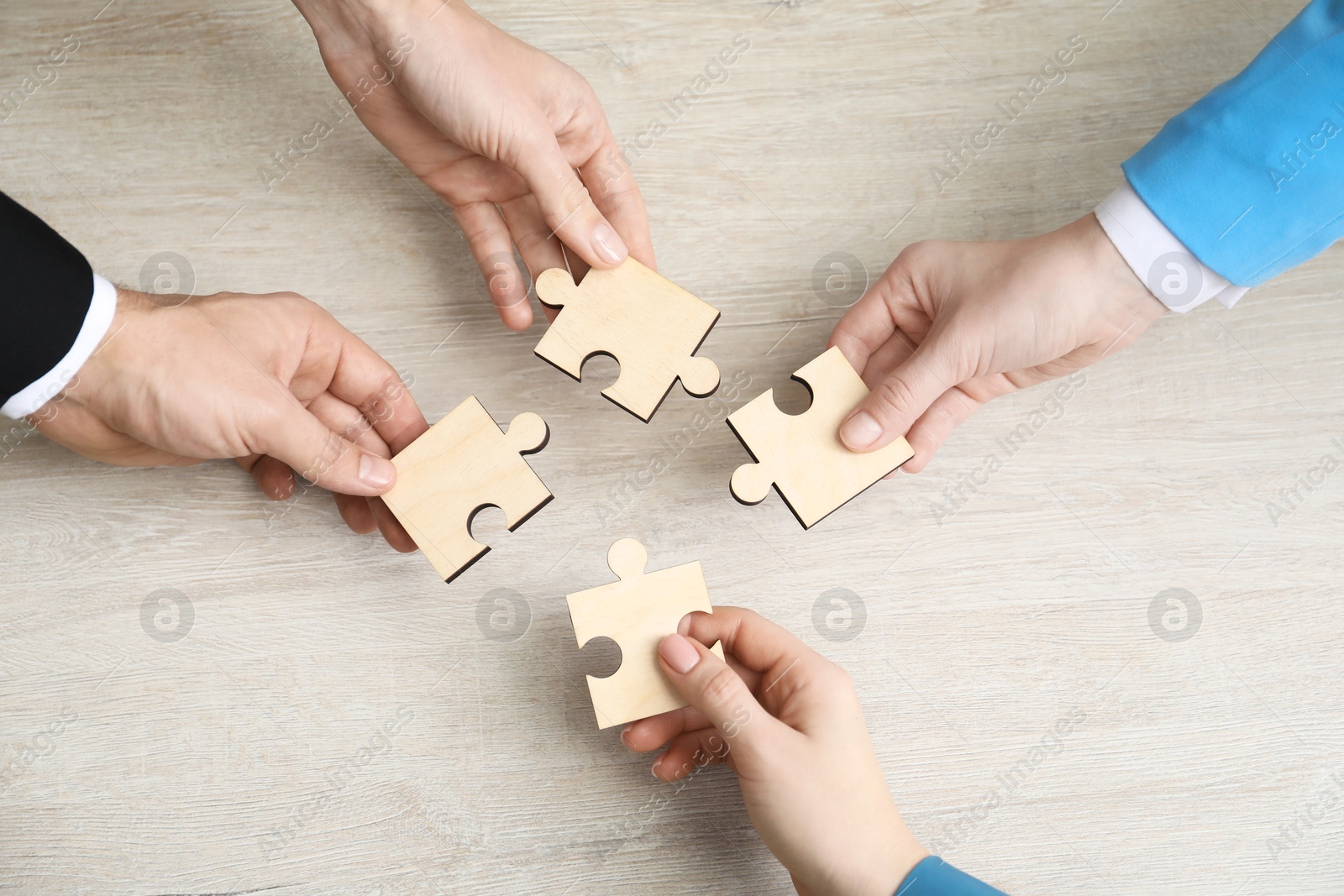 Photo of Teamwork. Group of people putting puzzle pieces together at wooden table, top view