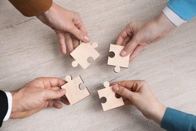 Photo of Teamwork. Group of people putting puzzle pieces together at wooden table, top view