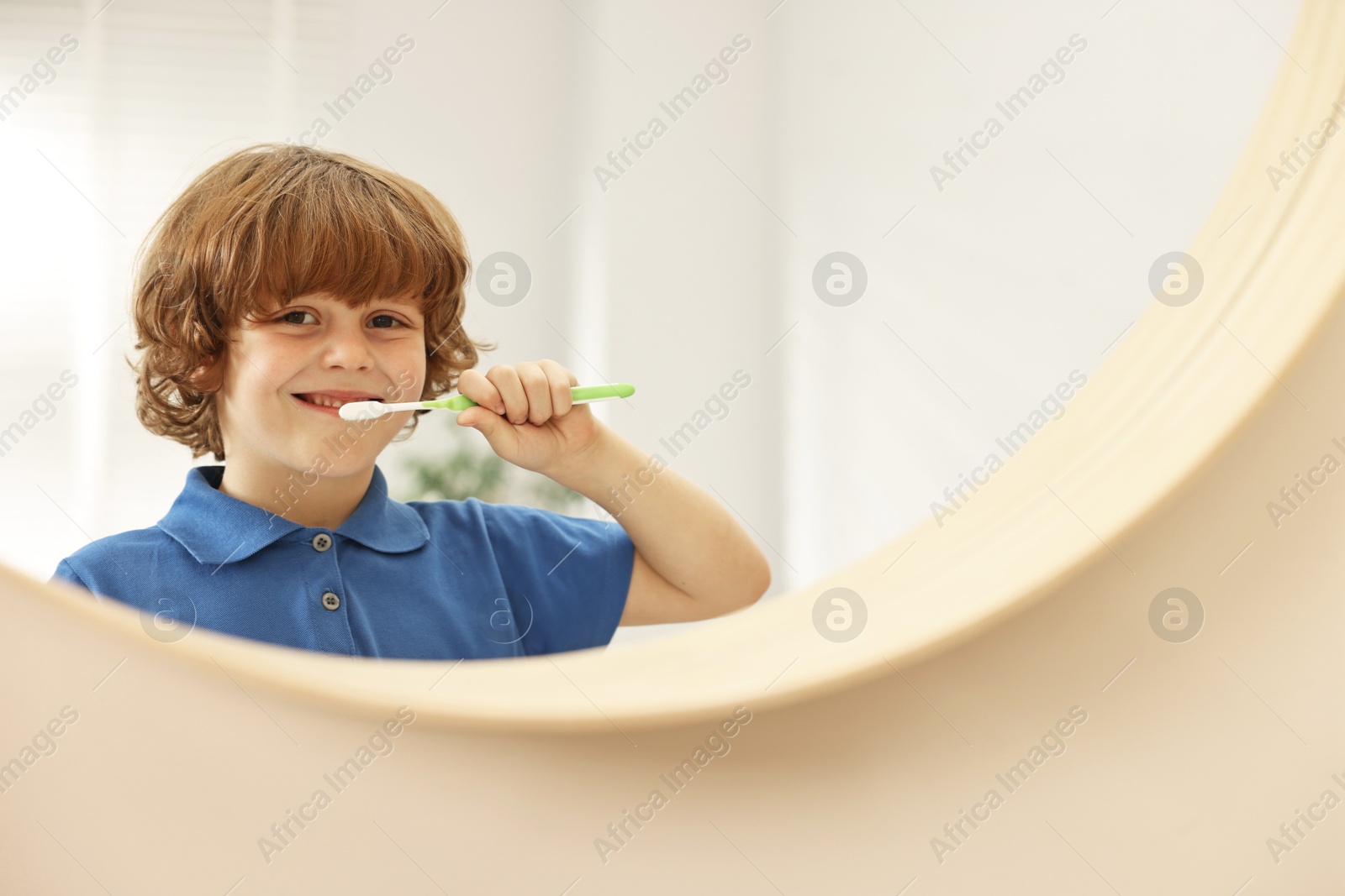 Photo of Cute boy brushing his teeth near mirror indoors