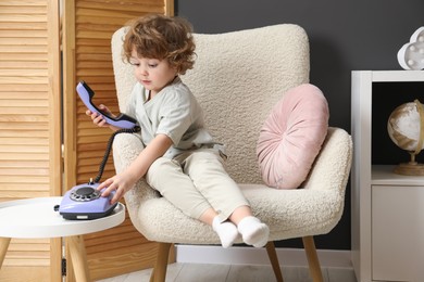 Photo of Cute little boy with telephone in armchair indoors