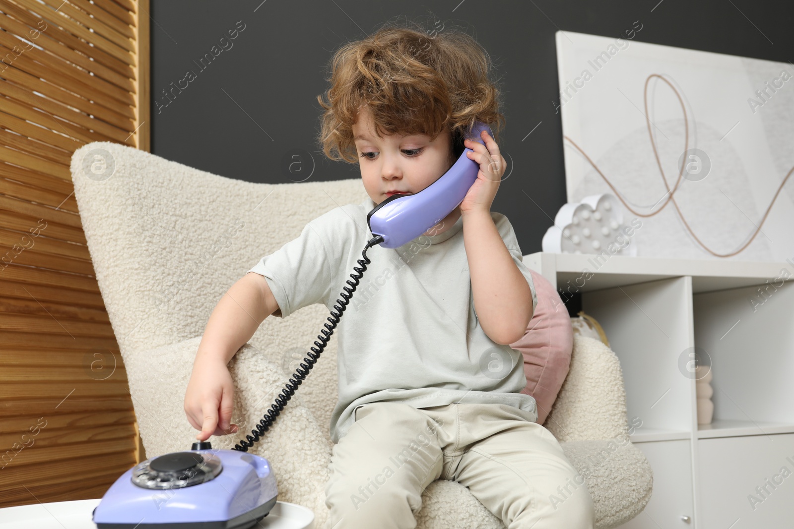 Photo of Cute little boy with telephone in armchair indoors