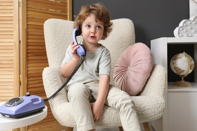 Photo of Cute little boy with telephone in armchair indoors