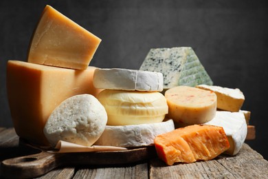 Photo of Different types of cheese on wooden table against dark background, closeup