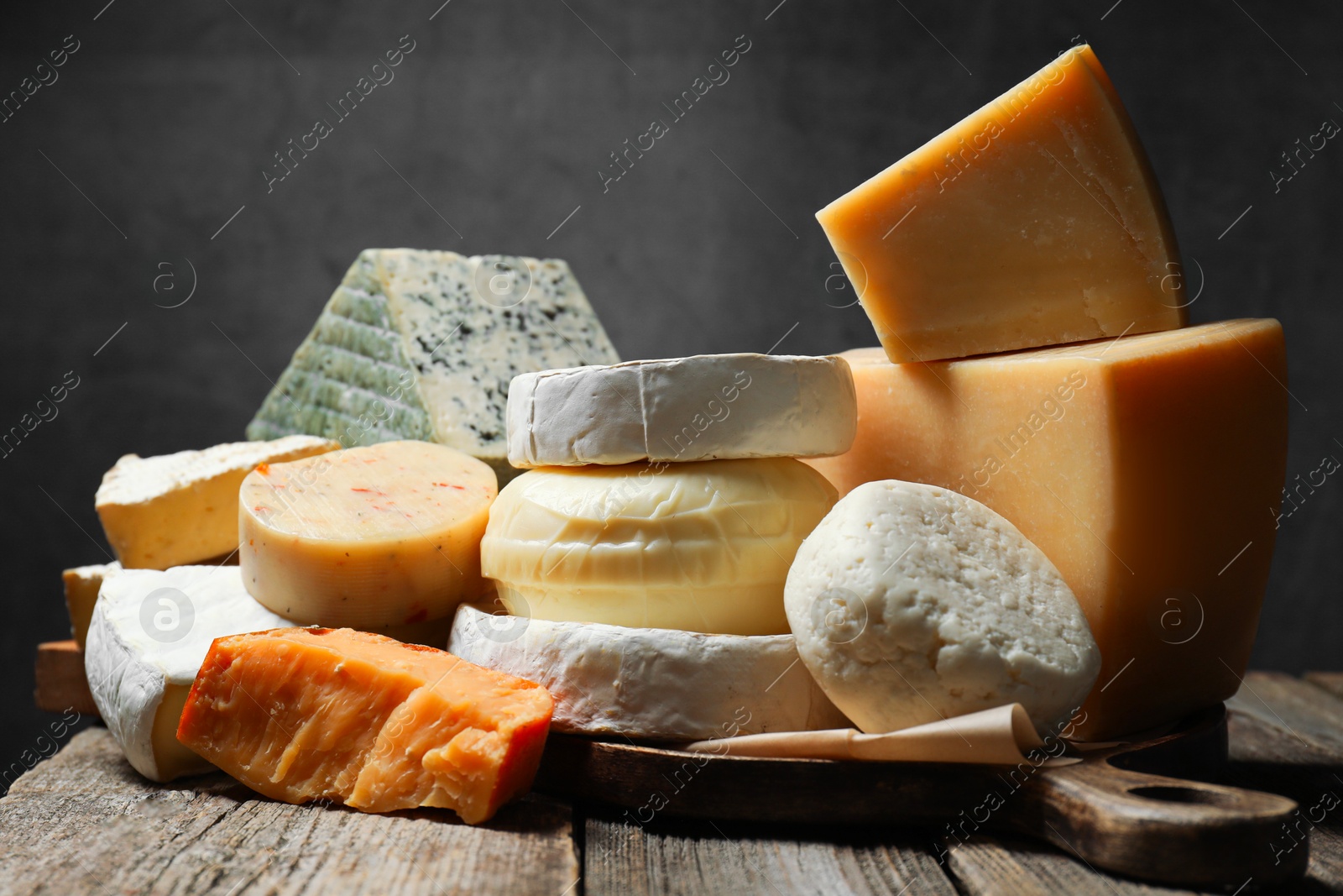 Photo of Different types of cheese on wooden table against dark background, closeup