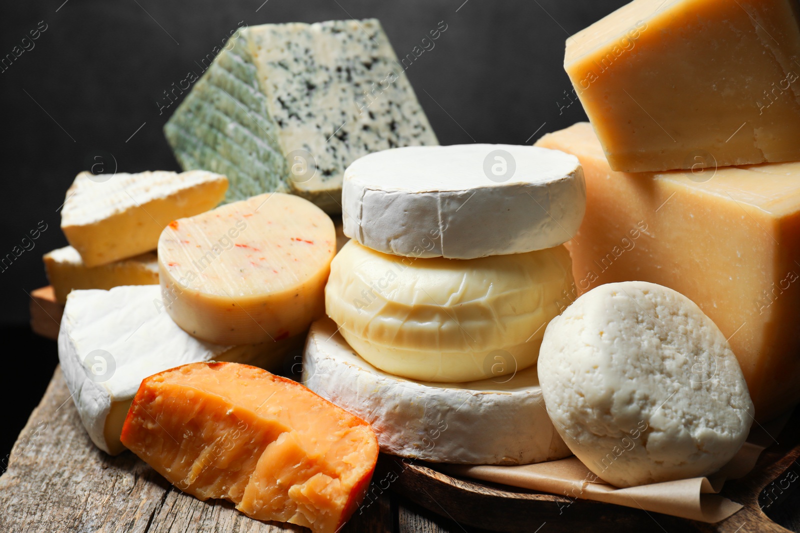 Photo of Different types of cheese on wooden table against dark background, closeup