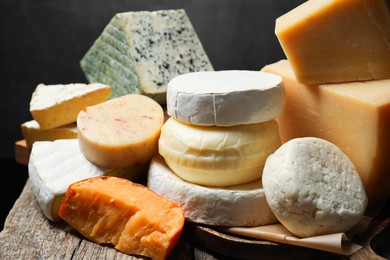 Photo of Different types of cheese on wooden table against dark background, closeup