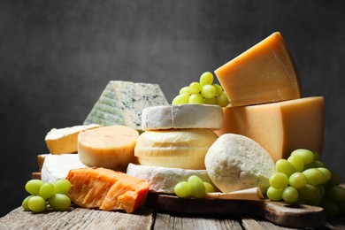 Photo of Different types of cheese and grapes on wooden table against dark background, closeup