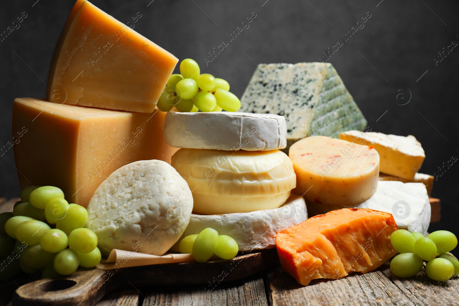 Photo of Different types of cheese and grapes on wooden table against dark background, closeup