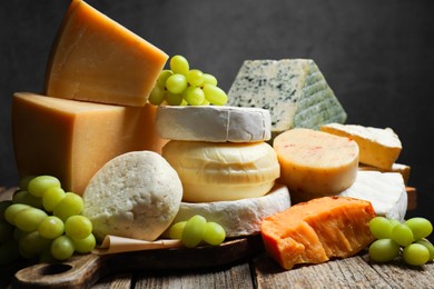 Photo of Different types of cheese and grapes on wooden table against dark background, closeup