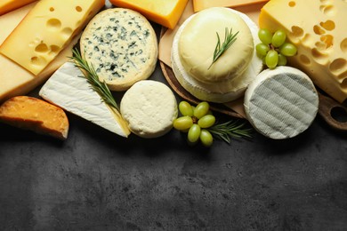 Photo of Different types of cheese, rosemary and grapes on dark textured table, flat lay. Space for text