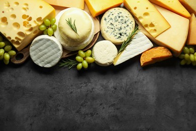 Photo of Different types of cheese, rosemary and grapes on dark textured table, flat lay. Space for text