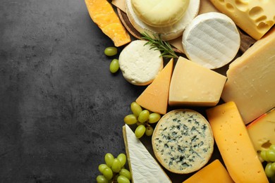 Photo of Different types of cheese, rosemary and grapes on dark textured table, flat lay. Space for text