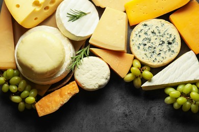 Photo of Different types of cheese, rosemary and grapes on dark textured table, flat lay