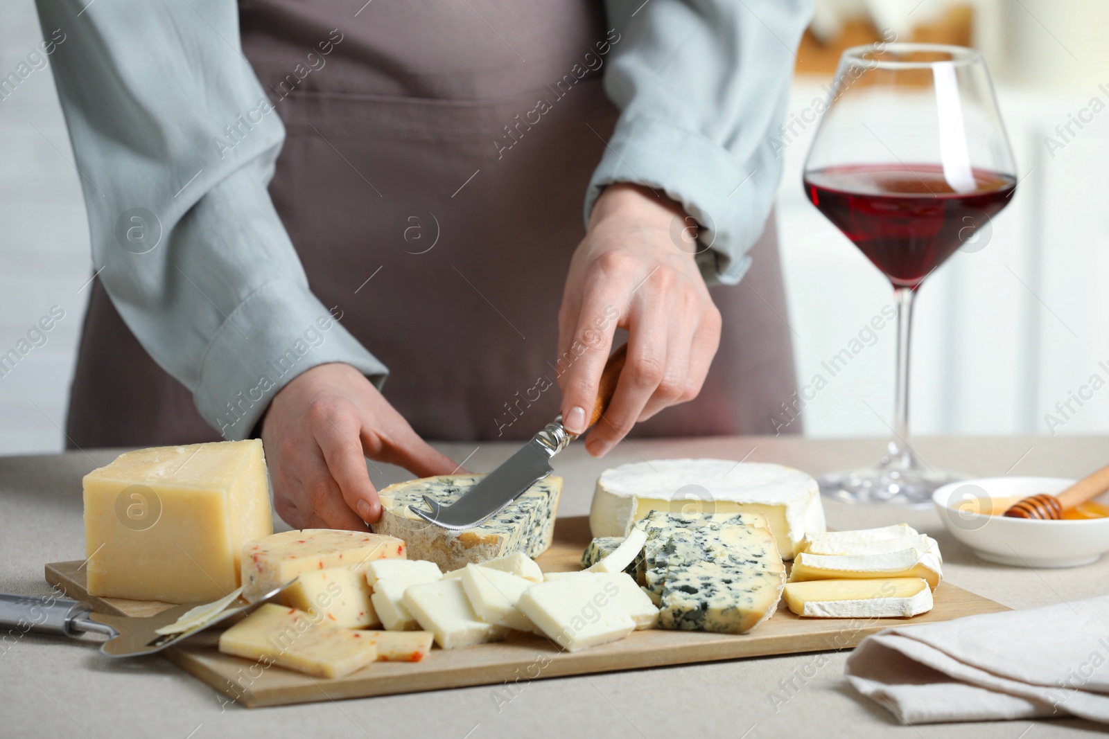 Photo of Woman slicing delicious cheese at light textured table indoors, closeup