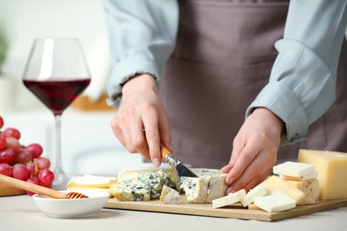 Photo of Woman slicing delicious cheese at light textured table indoors, closeup