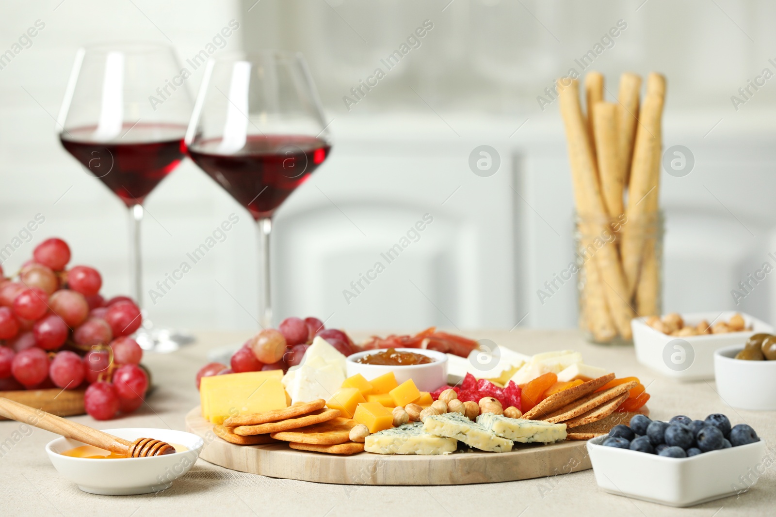 Photo of Different types of cut cheese and other snacks on light textured table, closeup