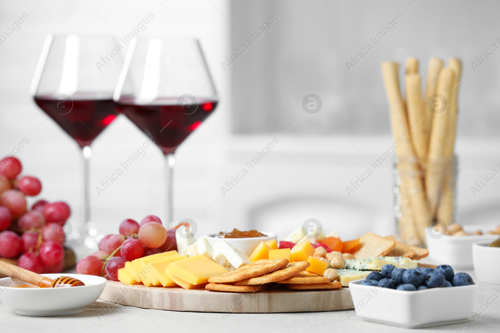 Photo of Different types of cut cheese and other snacks on light textured table, closeup