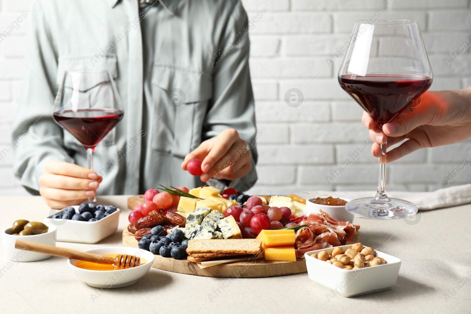 Photo of Women holding glasses of wine at light grey table with different snacks indoors, closeup