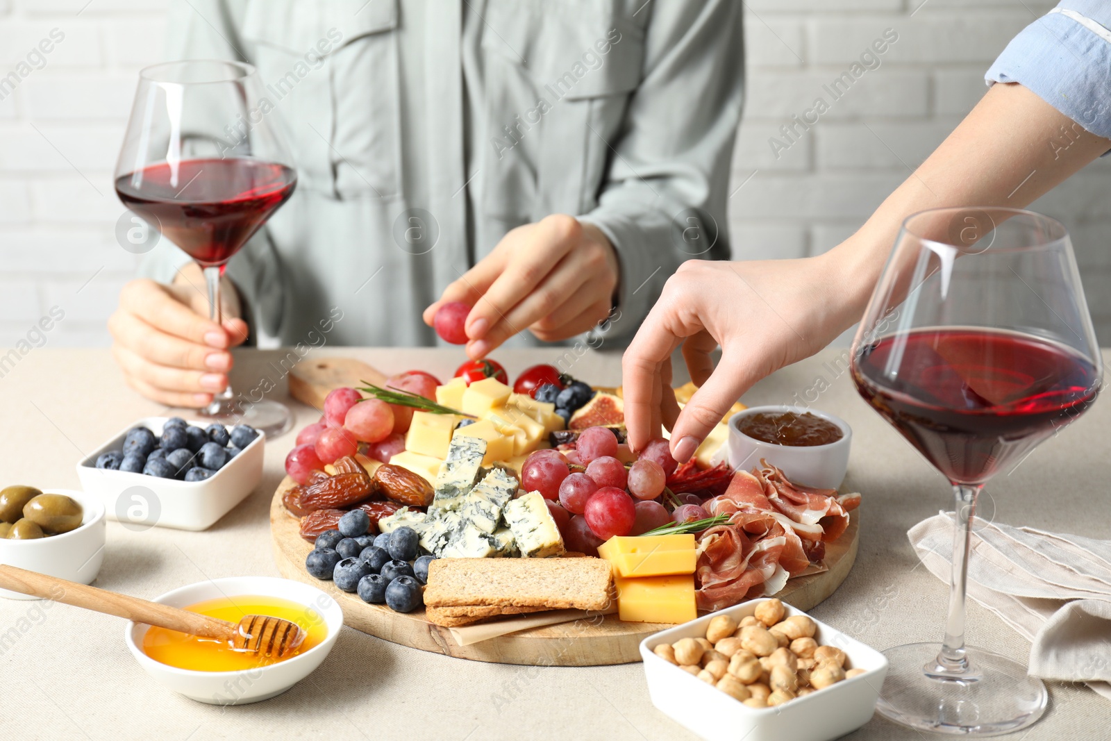 Photo of Women enjoying different snacks and wine during brunch at light grey table indoors, closeup