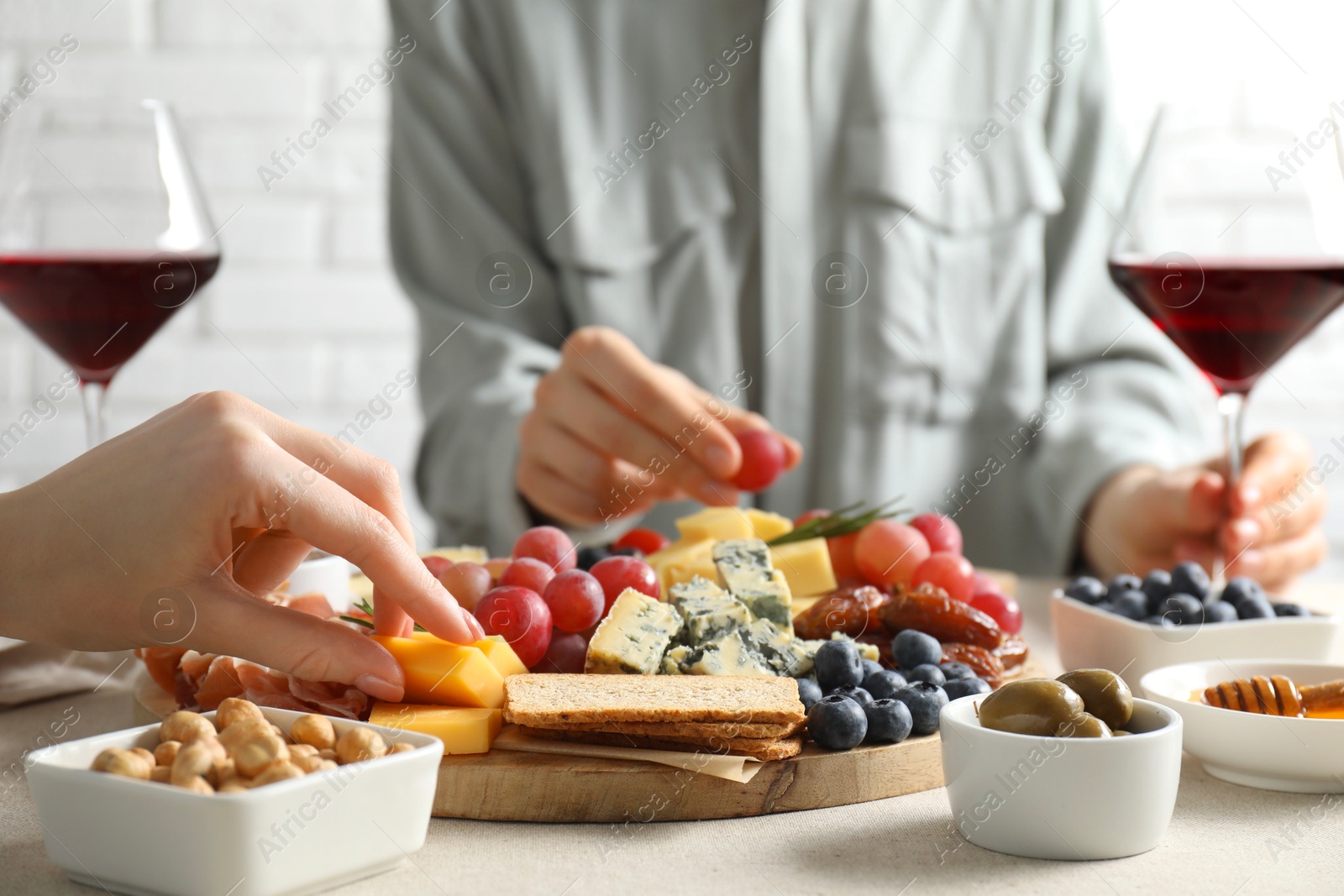 Photo of Women enjoying different snacks and wine during brunch at light grey table indoors, closeup