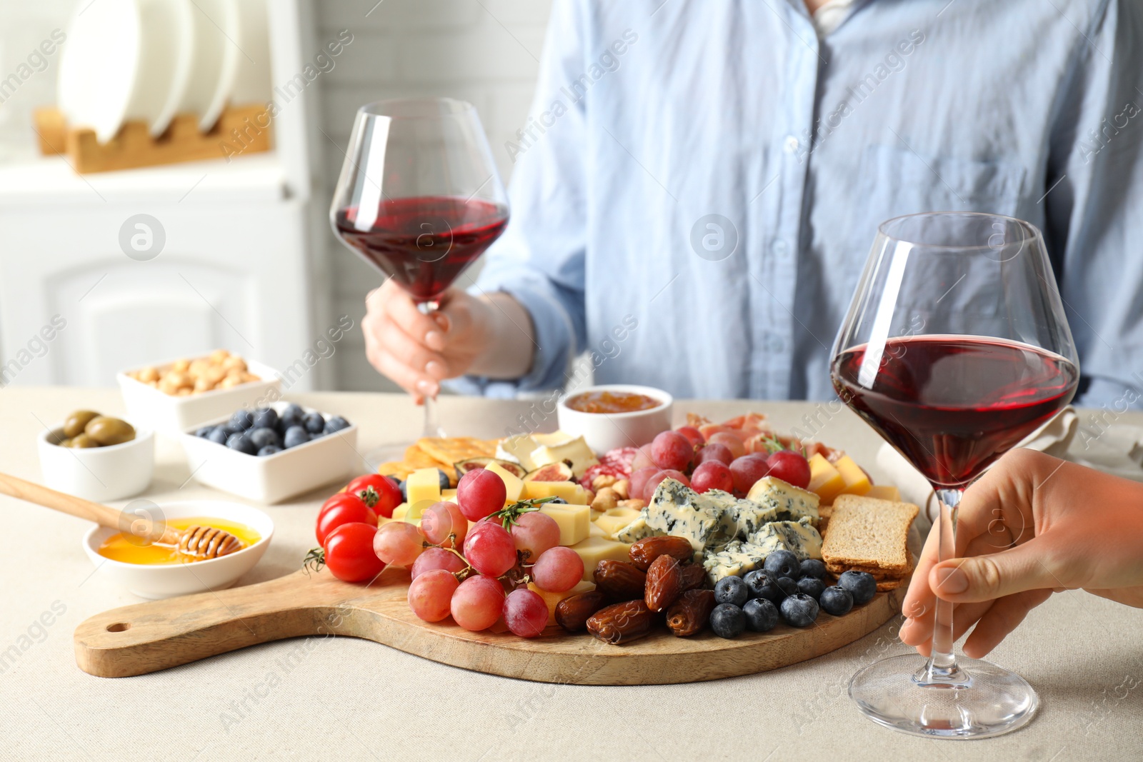 Photo of Women holding glasses of wine at light grey table with different snacks indoors, closeup