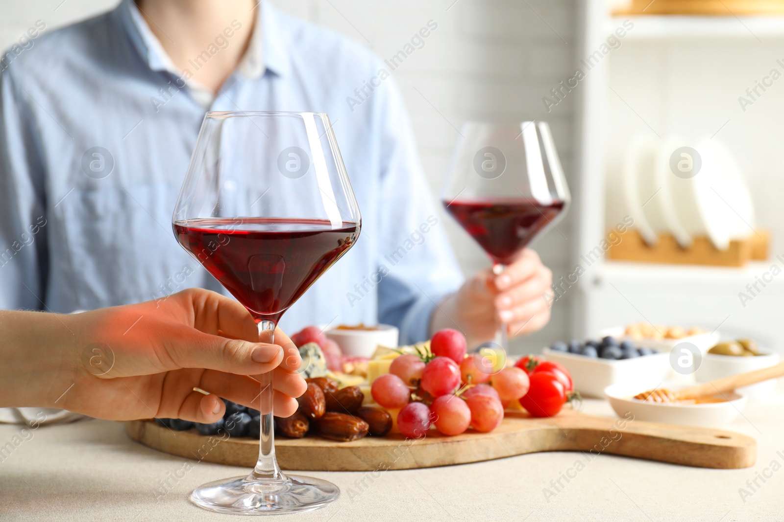 Photo of Women holding glasses of wine at light grey table with different snacks indoors, closeup